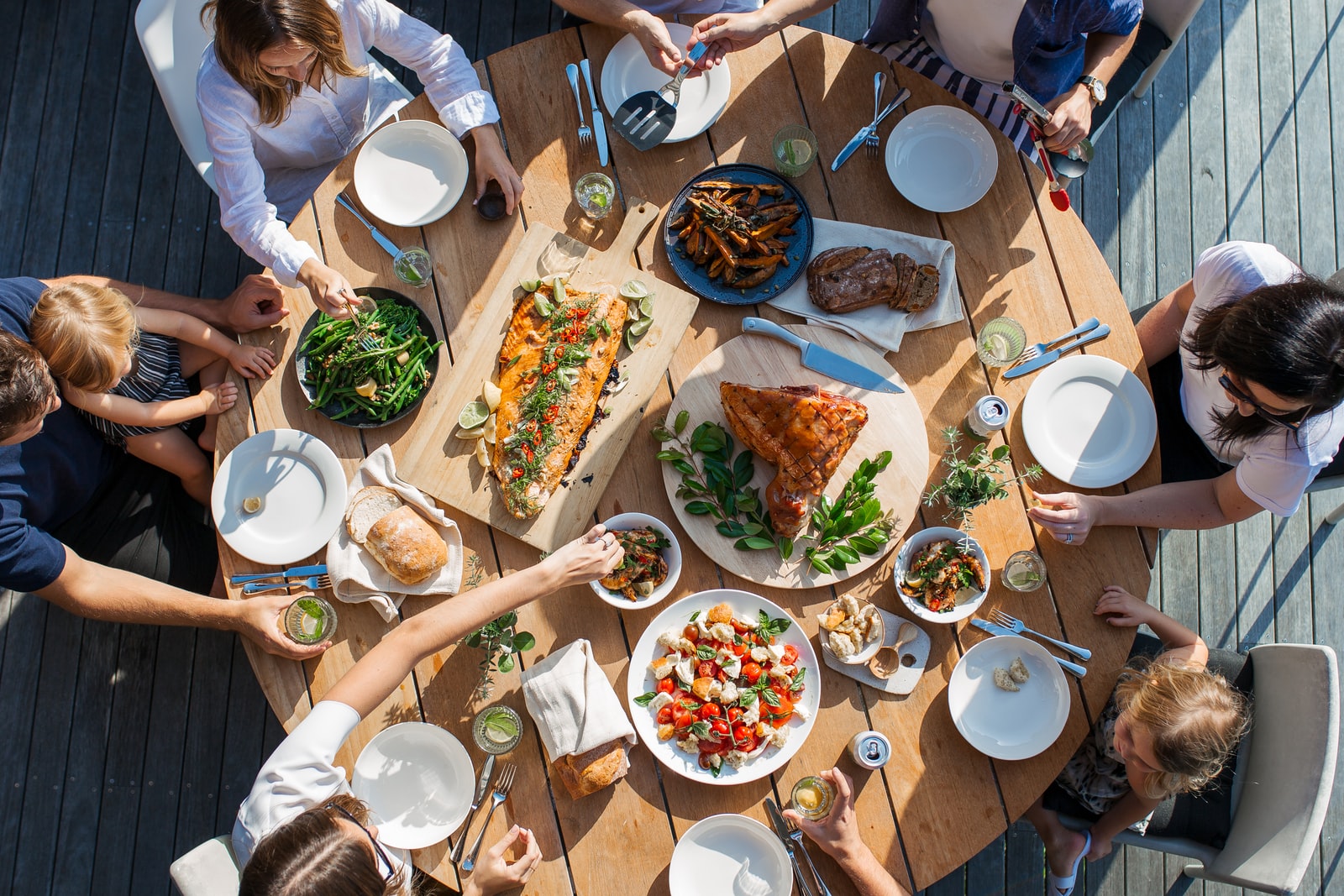 AD Technics - Bovenaanzicht van een groep mensen die rond een ronde houten tafel zitten en een verscheidenheid aan gerechten eten, waaronder salades, brood, geroosterd vlees en groenten. Overweeg bij dergelijke bijeenkomsten een koelcel van AD Technics om uw ingrediënten vers te houden.