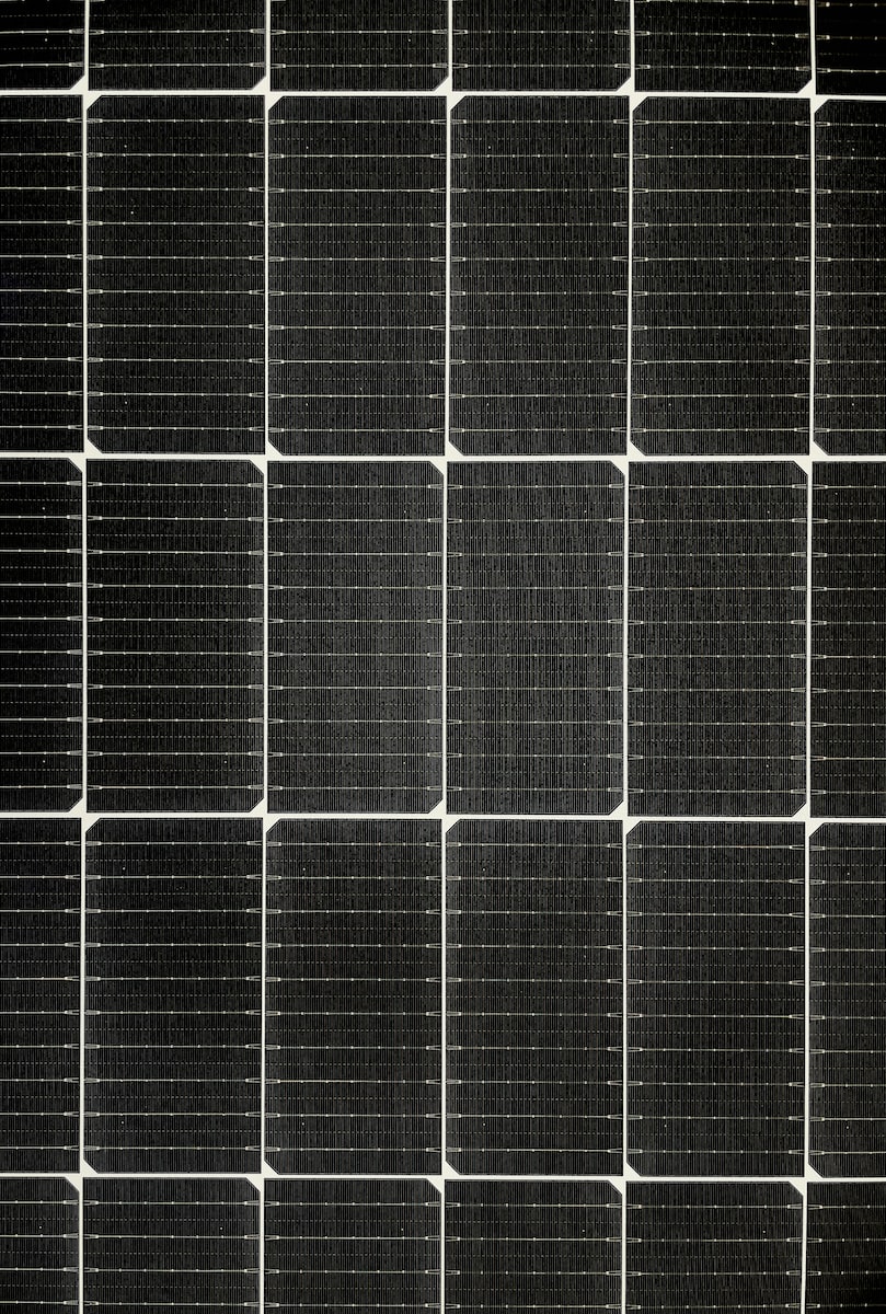 AD Technics - Close-up van een raster van zwarte zonnepanelen, met individuele rechthoekige cellen gerangschikt in een netjes patroon, waarin geavanceerde technologie wordt getoond, vaak gecombineerd met systemen zoals vloerverwarming voor verbeterde energie-efficiëntie.